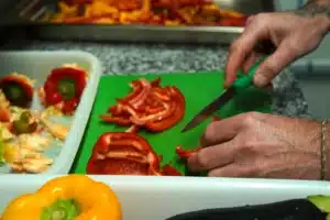 Découpe de poivrons rouges et jaunes dans le food truck pizza PIZZ'A YANN, garantissant des pizzas faites maison avec des produits frais.
